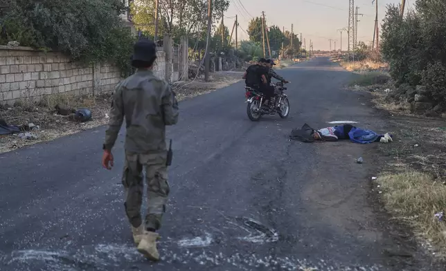 Syrian government forces pass next of a dead fighter from Druze militias, at Mazraa village on the outskirts of the city of Sweida, where clashes erupted between Sunni Bedouin clans and Druze militias, southern Syria, Monday, July 14, 2025. (AP Photo/Ghaith Alsayed)
