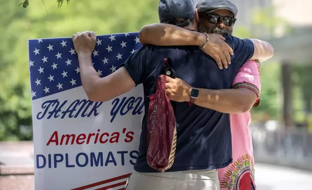 A man hugs former Foreign Service employee Bob Gilchrist, of Washington, left, as he holds a sign reading "Thank You America's Diplomats" outside the State Department headquarters, Friday, July 11, 2025, in Washington. (AP Photo/Mark Schiefelbein).