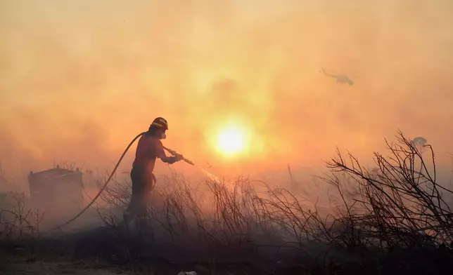 A firefighter tries to extinguish a wildfire as a helicopter flies, in the northwestern suburb of Kryoneri, in Athens, Greece, Saturday, July 26, 2025. (AP Photo/Yorgos Karahalis)