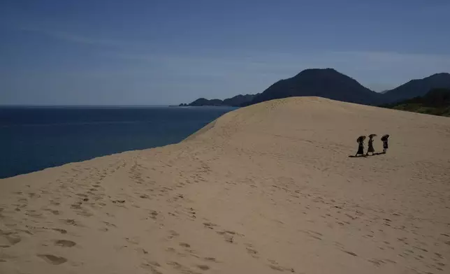 Visitors holding parasols walk through the Tottori Sand Dunes in Tottori Prefecture, Monday, July 28, 2025. (AP Photo/Louise Delmotte)