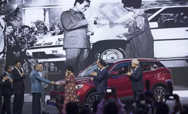 FILE - Malaysia Prime Minister Mahathir Mohamad, left, hands the keys to his wife Siti Hasmah as it is shown on the screen when he launched the first Proton car 35 years ago during the launch of Proton new SUV in Kuala Lumpur, Malaysia, Dec. 12, 2018. (AP Photo/Vincent Thian,File)