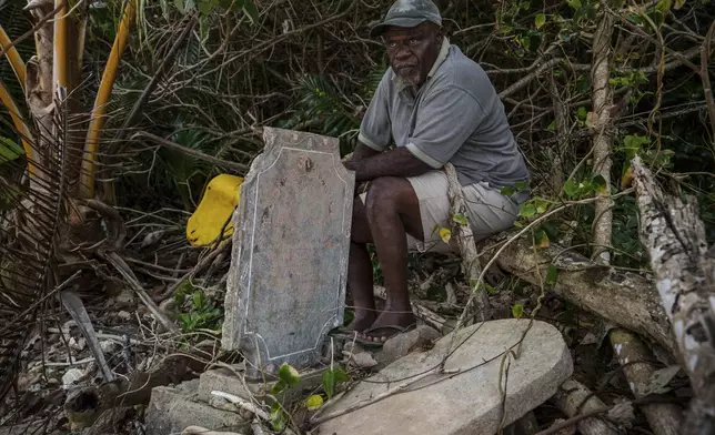 Village chief Amos Kalsont sits at his brother's grave on Pele Island, Vanuatu, just feet from the shoreline, where another headstone has been washed up on top of the site Friday, July 18, 2025. (AP Photo/Annika Hammerschlag)