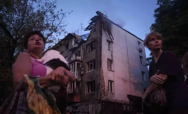 Local residents stand outside of their house which was heavily damaged by a Russian strike in Kyiv, Ukraine, on Thursday, July 10, 2025. (AP Photo/Evgeniy Maloletka)