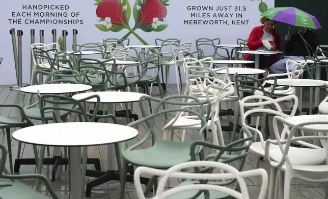 People eat their strawberries under an umbrella outdoors as the start of play is delayed due to rain during the Wimbledon Tennis Championships in London, Wednesday, July 2, 2025.(AP Photo/Kirsty Wigglesworth)