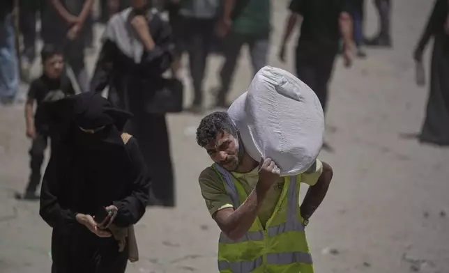 Palestinians carry bags of flour distributed by the World Food Programme (WFP) in Gaza City, northern Gaza Strip, Saturday, July 12, 2025. (AP Photo/Jehad Alshrafi)