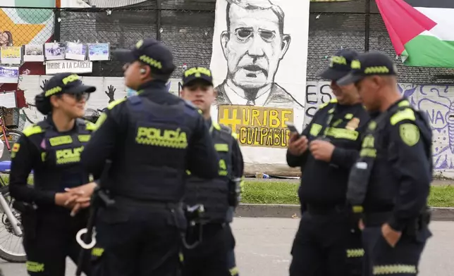 Police stand in front of a banner reading in Spanish "Uribe guilty" displayed by opponents of former President Alvaro Uribe outside the court where a verdict is expected in his trial for witness tampering in Bogota, Colombia, Monday, July 28, 2025. (AP Photo/Fernando Vergara)