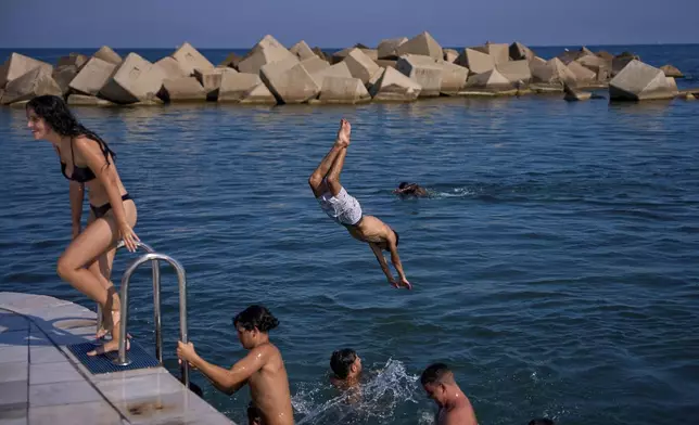 Swimmers jump into the water on a hot day in Barcelona, Spain, Tuesday, July 1, 2025. (AP Photo/Emilio Morenatti)
