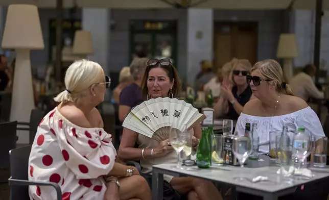 A woman cools herself with a hand fan at a restaurant terrace during a heat wave in Madrid, Spain, Tuesday, July 1, 2025. (AP Photo/Manu Fernandez)