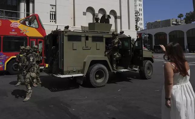 A person takes cell phone images of federal agents Monday, July 7, 2025, in Los Angeles. (AP Photo/Damian Dovarganes)