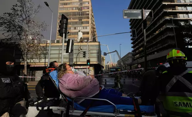 A woman lies on a stretcher after being evacuated from a burning building in Santiago, Chile, Thursday, July 10, 2025. (AP Photo/Esteban Felix)