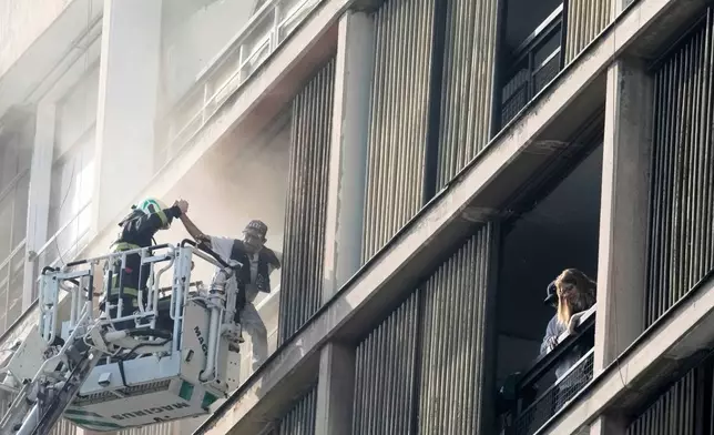 A firefighter rescues a man trapped inside a building on fire in Santiago Chile, Thursday, July 10, 2025. (AP Photo/Esteban Felix)