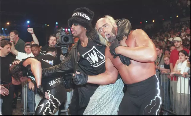 FILE - Basketball star Dennis Rodman, center, helps his wrestling tag team back to the ring, March 16, 1997, at the World Championship Wrestling pay-per-view event at the North Charleston Coliseum in Charleston, S.C. At left is Randy "Macho Man" Savage, and at right is his partner Hulk Hogan. (AP Photo/Paula Illingworth, File)