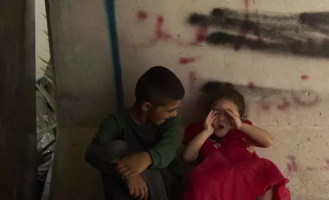 Siblings mimic the sound of sirens that alert incoming rocket and missiles, inside an open concrete bomb shelter in Al-Zarnug, an unrecognized Bedouin community in the Negev Desert, southern Israel, Wednesday, July 2, 2025. (AP Photo/Maya Alleruzzo)