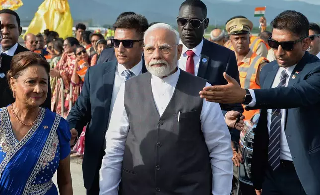 India's Prime Minister Narendra Modi, center, walks with Trinidad and Tobago Prime Minister Kamla Persad-Bissessar, dressed in traditional Indian attire, left, upon his arrival at Piarco International Airport in Piarco, Trinidad and Tobago, Thursday, July 3, 2025. (AP Photo/Jermaine Cruickshank)
