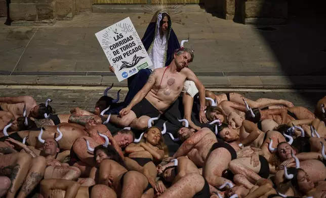 Animal rights activists, their bodies covered in blood, take part in a protest ahead of the San Fermin Festival in Pamplona, northern Spain, on Saturday, July 5, 2025. The activist dressed as the Virgin Mary holds a placard reading ''Bullfighting is a sin''. (AP Photo/Miguel Oses)