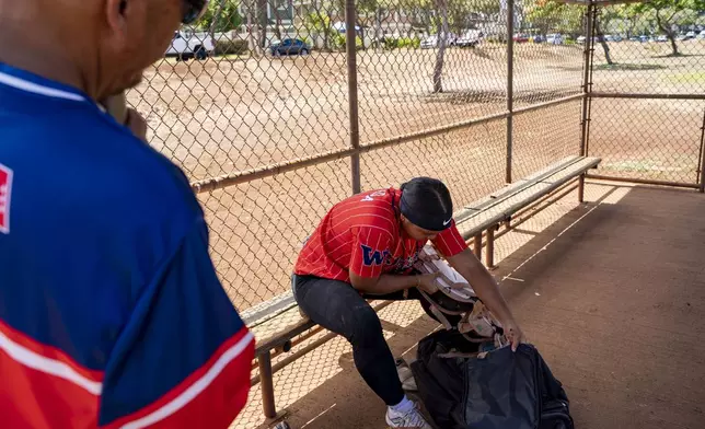 Tommy Uyeda, left, watches his daughter Ry-n, puts away her softball gear after practice, Friday, July 11, 2025, in Waianae, Hawaii. (AP Photo/Mengshin Lin)