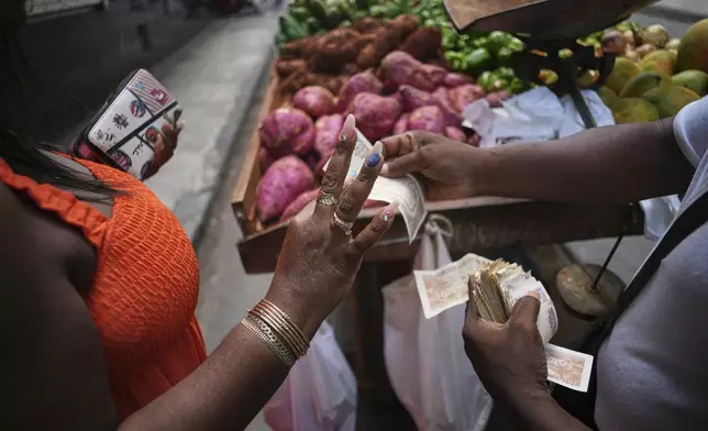 Maite Hernandez, donning long, decorated nails, takes her change from a vegetable vendor, in Havana, Cuba, Saturday, July 5, 2025. (AP Photo/Ramon Espinosa)