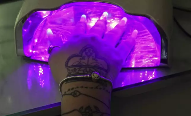 Mariam Camila Sosa places her hand under a UV lamp to speed dry her manicured nails at a home-run nail salon, in Havana, Cuba, Tuesday, June 24, 2025. (AP Photo/Ramon Espinosa)