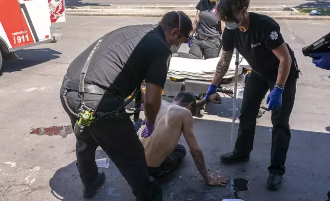 FILE - Salem Fire Department Capt. Matt Brozovich, left, and Falck Northwest ambulance personnel help treat a man experiencing heat exposure during a heat wave in Salem, Ore., June 26, 2021. (AP Photo/Nathan Howard, File)