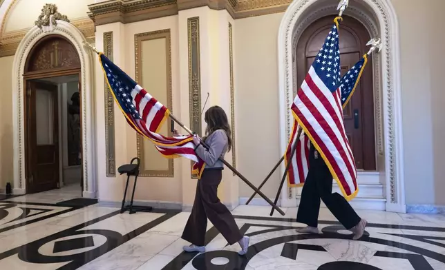 House staffers carry American flags through a corridor outside the House chamber which will be used for a ceremony with Speaker of the House Mike Johnson, R-La., after final passage of President Donald Trump's signature bill of tax breaks and spending cuts, at the Capitol in Washington, Thursday, July 3, 2025. (AP Photo/J. Scott Applewhite)