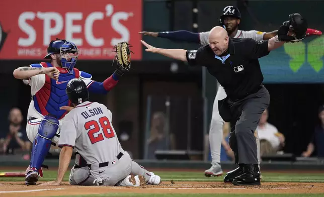 Texas Rangers catcher Jonah Heim, left, holds onto the ball after a collision at the plate with Atlanta Braves' Matt Olson (28) as umpire Mike Estabrook, right, makes a call that would be overturned after a video review in the first inning of a baseball game Saturday, July 26, 2025, in Arlington, Texas. (AP Photo/Tony Gutierrez)