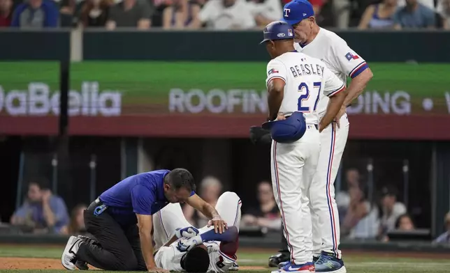 Texas Rangers athletic trainer Matt Lucero, left, third base coach Tony Beasley (27) and manager Bruce Bochy, right, check on Marcus Semien (2) after Semien was hit by a pitch in the third inning of a baseball game against the Atlanta Braves Saturday, July 26, 2025, in Arlington, Texas. (AP Photo/Tony Gutierrez)