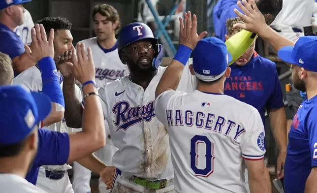 Texas Rangers' Adolis Garcia, center, celebrates with the team after scoring on a Evan Carter triple in the second inning of a baseball game against the Atlanta Braves Saturday, July 26, 2025, in Arlington, Texas. (AP Photo/Tony Gutierrez)