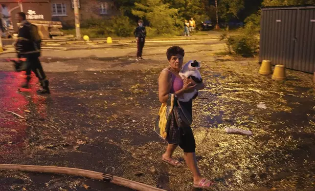 A woman carries her cat as she walks on a street at the site of a residential building that was damaged after a Russian attack, Ukraine, early Thursday, July 10, 2025. (AP Photo/Efrem Lukatsky)