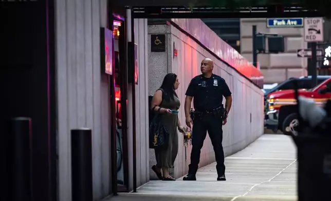 A New York police officer talks with a woman as she exits a Manhattan office building where two people were shot including a police officer, Monday, July 28, 2025, in New York. (AP Photo/Angelina Katsanis)