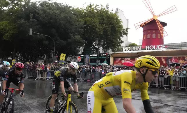 Slovenia's Tadej Pogacar, wearing the overall leader's yellow jersey, rides past the Moulin Rouge cabaret during the last stage of the Tour de France cycling race between Mantes-la-Ville and Paris, Sunday, July 27, 2025 in Paris (AP Photo/Michel Euler)