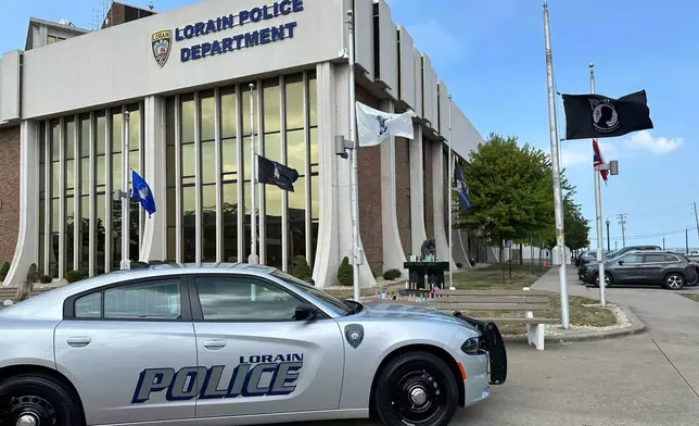 Candles sit on a memorial and flags fly at half-staff outside the police department in Lorain, Ohio, on Thursday, July 24, 2025, a day after three officers were wounded in a shooting ambush. (AP Photo/John Seewer)