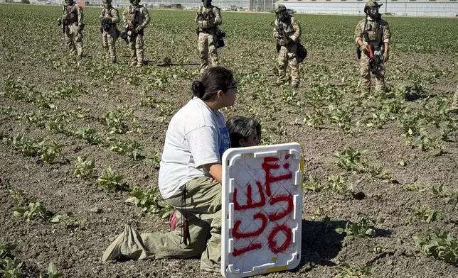 A demonstrator kneels in front of federal agents in a farm field during an immigration raid in Camarillo, Calif., Thursday, July 10, 2025. (AP Photo/Michael Owen Baker)