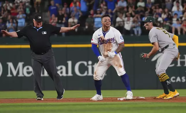 Texas Rangers' Cody Freeman, center, reacts in front of Athletics shortstop Jacob Wilson (5) at second base after hitting a double that scored teammate Josh Smith during the fifth inning of a baseball game, Monday, July 21, 2025, in Arlington, Texas. (AP Photo/LM Otero)