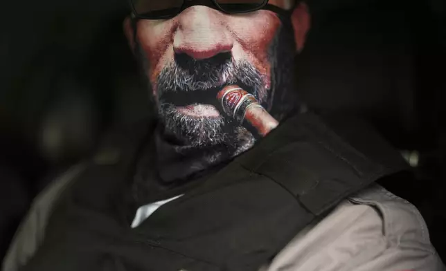 An immigration official wears a face mask depicting a cigar and beard as he waits to transport detained immigrants Wednesday, July 23, 2025, in Baldwin Park, Calif. (AP Photo/Gregory Bull)