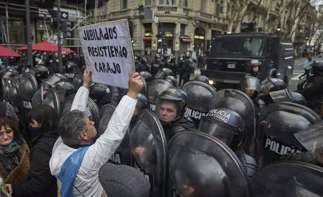A demonstrator holds up a sign with a message that reads in Spanish: "Pensioners resisting," in front of a police cordon during a weekly protest demanding better pensions for retirees in Buenos Aires, Argentina, Wednesday, July 23, 2025. (AP Photo/Victor R. Caivano)