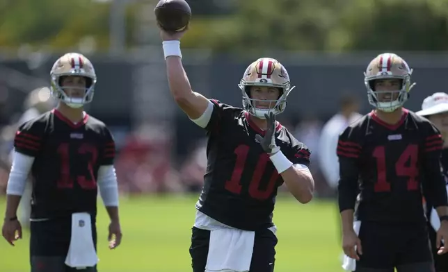 San Francisco 49ers quarterback Mac Jones (10) throws a pass between quarterbacks Brock Purdy (13) and Tanner Mordecai (14) during practice at the team's NFL football training camp, Wednesday, July 23, 2025, in Santa Clara, Calif. (AP Photo/Jeff Chiu)