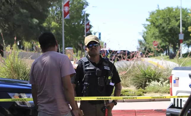 An officer talks to a delivery driver at a roadblock on the University of New Mexico campus where two people were shot, one of them fatally, in the early morning hours in Albuquerque, N.M., on Friday, July 25, 2025. (AP Photo/Susan Montoya Bryan)