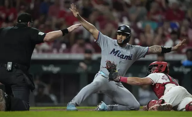 Cincinnati Reds catcher Tyler Stephenson, right, looks to umpire Chris Conroy, left, as Miami Marlins' Agustín Ramírez, center, is safe at home plate on a single by Liam Hicks during the fifth inning of a baseball game in Cincinnati, Monday, July 7, 2025. The Reds challenged but the call on the field was upheld. (AP Photo/Carolyn Kaster)
