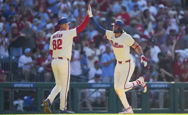 Philadelphia Phillies' Alec Bohm, right, high-fives third base coach Dusty Wathan (62) after hitting a two-run home run during the sixth inning of a baseball game against the Cincinnati Reds, Saturday, July 5, 2025, in Philadelphia. (AP Photo/Derik Hamilton)