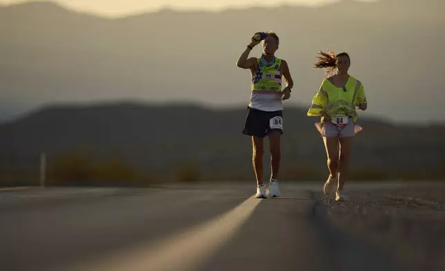 Danny Westergaard, left, cools of with water with pacing help from daughter Madison Westergaard as the sun rises during the Badwater 135 Ultramarathon, Tuesday, July 8, 2025, in Death Valley National Park, Calif. (AP Photo/John Locher)