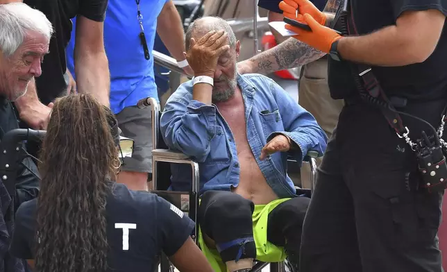 Michael Pimentel, center, a resident at the Gabriel House assisted living facility, in Fall River, Mass., receives assistance from an emergency medical worker, right, outside a temporary shelter, Monday, July 14, 2025, in Fall River, following a fire that started late Sunday. (AP Photo/Steven Senne)