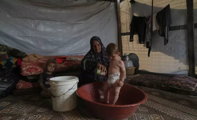 Siham Abu Hadayed, 52, cools off with water her 11-month-old grandchild Yasser in their tent at a camp for displaced people in Khan Younis, southern Gaza Strip, Tuesday, July 1, 2025. (AP Photo/Abdel Kareem Hana)