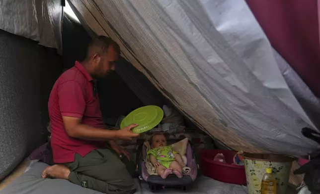 Issam Abu Hadayed, 28, tries to cool off her 5-month-old baby Amira, with a plastic plate as they sit in their tent at a camp for displaced people in Khan Younis, southern Gaza Strip, Tuesday, July 1, 2025. (AP Photo/Abdel Kareem Hana)