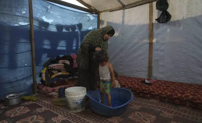 Rida Abu Hadayed, 32, cools off with water her 2-year-old daughter Azhar in their tent at a camp for displaced people in Khan Younis, southern Gaza Strip, Tuesday, July 1, 2025. (AP Photo/Abdel Kareem Hana)