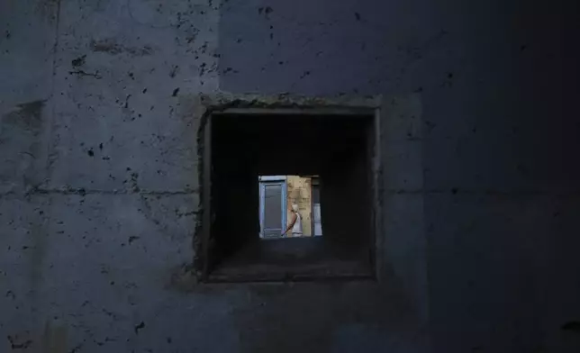 A woman is seen through a military battle position from a wall next to the U.N buffer zone that divided the south, Greek Cypriots, and the north, Turkish Cypriot breakaway controlled areas in divided capital Nicosia, Cyprus, Thursday, July 17, 2025. (AP Photo/Petros Karadjias)