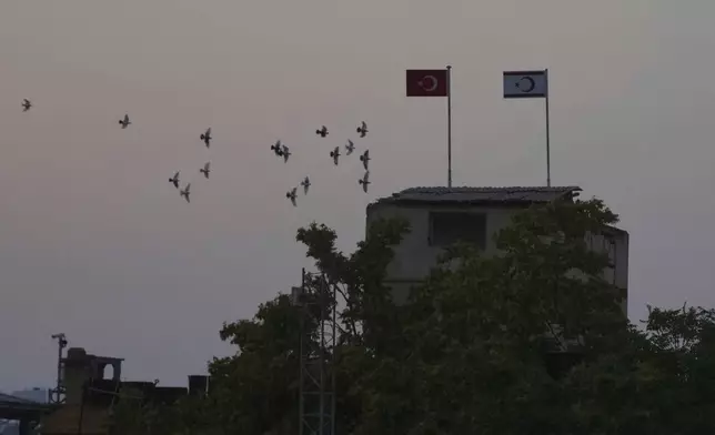 Birds fly behind a Turkish military guard post with a Turkish, left, and Turkish Cypriot breakaway flags next of a U.N buffer zone in divided capital Nicosia, Cyprus, Thursday, July 17, 2025. (AP Photo/Petros Karadjias)