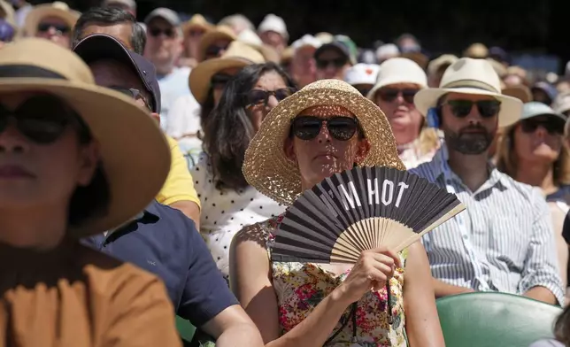 A spectator fans herself to keep cool as she watches Taylor Fritz of the U.S. play Spain's Carlos Alcaraz in a men's singles semifinal at the Wimbledon Tennis Championships in London, Friday, July 11, 2025. (AP Photo/Kin Cheung)