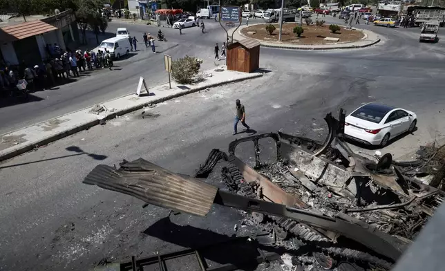 Residents walk past a burned-out military vehicle after last week's sectarian clashes in the Druze-majority town of Sweida, Syria, on Friday, July 25, 2025. (AP Photo/Omar Sanadiki)