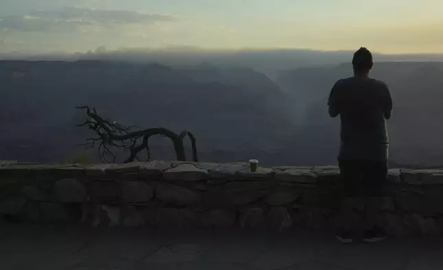 A tourist watches from a South Rim overlook as the early morning smoke from the Dragon Bravo Fire moves over the Grand Canyon from the North Rim Tuesday, July 15, 2025, in Grand Canyon National Park, Ariz. (AP Photo/Ross D. Franklin)