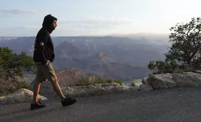 A tourist takes in the morning sunrise from the South Rim as smoke from the Dragon Bravo Fire moves over the Grand Canyon from the North Rim Tuesday, July 15, 2025, in Grand Canyon National Park, Ariz. (AP Photo/Ross D. Franklin)